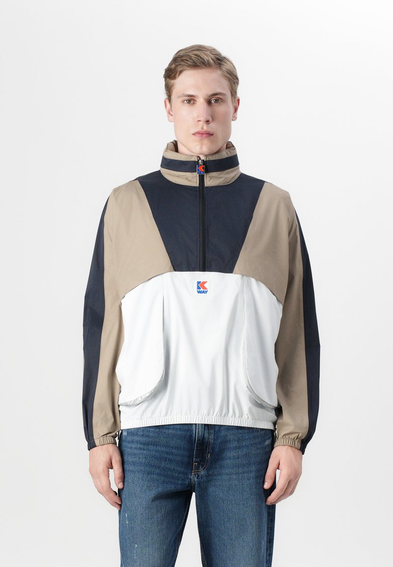 Lett anorakkjakke i beige, marineblå og hvit, med høy krage, halv glidelås og elastiske mansjetter. Logo på brystet.