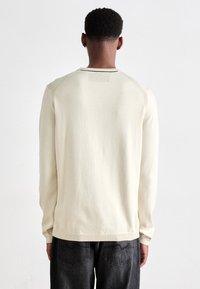Suéter de punto crema con mangas largas, escote redondo y espalda texturizada. Acompañado de jeans de mezclilla oscura con bolsillos traseros.