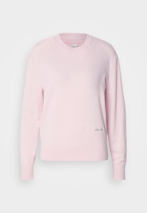 Svetlo roza pulover, narejen iz mehke pletene tkanine. Ima okroglo ovratnik in dolge rokave, z majhnim zelenim logotipom na spodnjem levem delu.