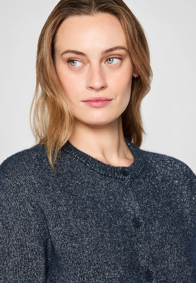 Marineblauer Pullover mit rundem Halsausschnitt, geripptem Kragen und zwei dunklen Knöpfen. Strukturiertes Material mit subtiler Glanzwirkung und lässiger Passform.
