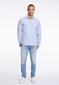 Lange mouw gestreept shirt in blauw en wit, met knoopsluiting, kraag, en een borstzak; gecombineerd met licht gewassen spijkerbroek en witte sneakers.