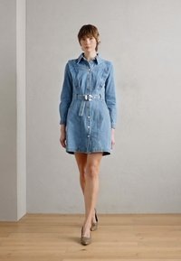 Lyseblå denimkjole med en tilpasset midje, knappelukking foran og lange ermer. Har belte, rund krage og en lett utsvingt skjørt.