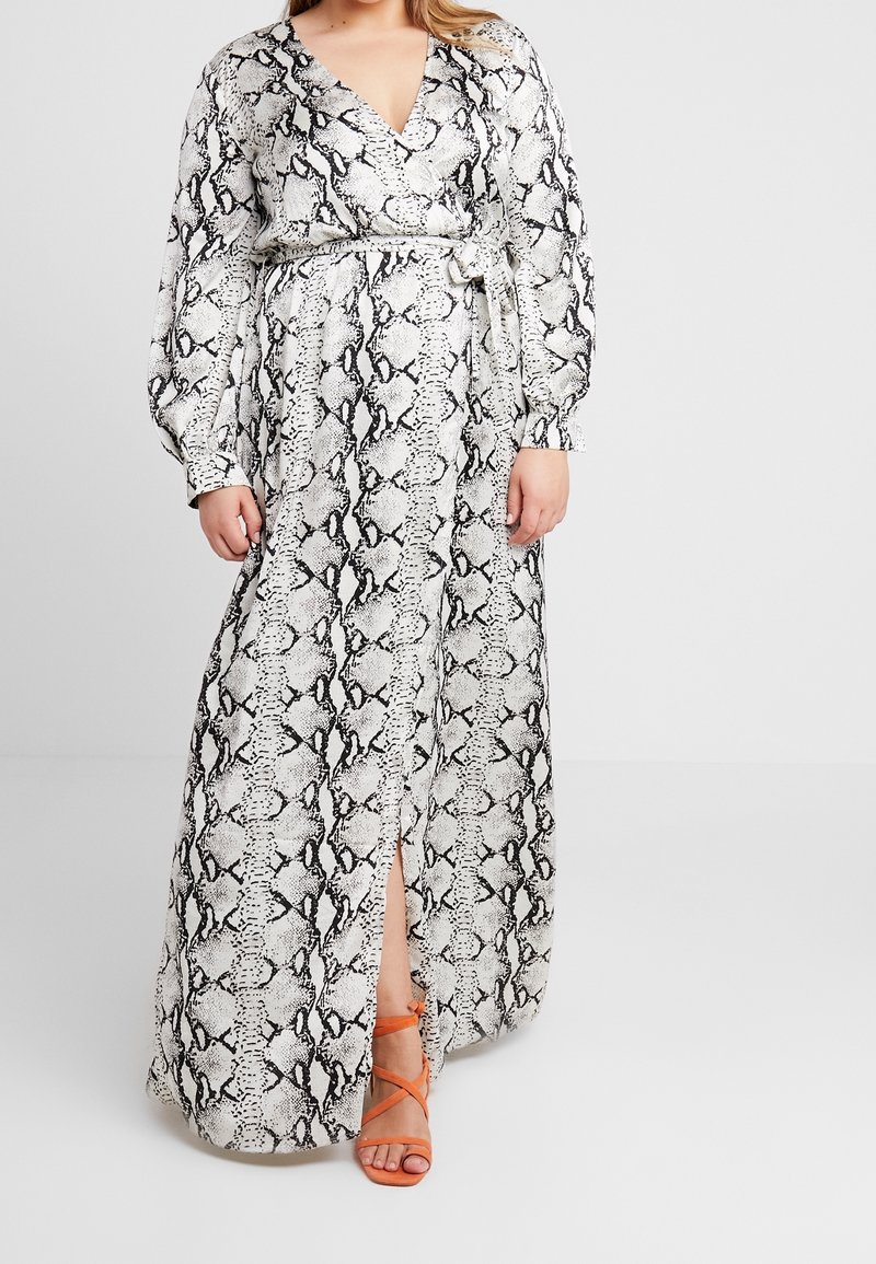 Femme portant une robe portefeuille à manches longues et longueur cheville avec imprimé serpent, une fente devant et des sandales orange à lanières.