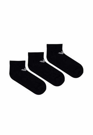 Tre calzini neri alla caviglia con un piccolo logo bianco sul lato disposti in fila su uno sfondo bianco.