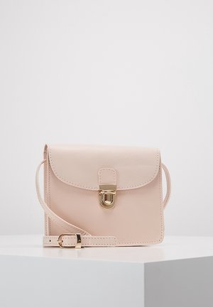 Una borsa a tracolla di colore rosa chiaro con una chiusura dorata e una tracolla regolabile è appoggiata su una superficie bianca, mettendo in mostra il suo design minimalista e la finitura elegante.