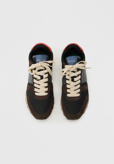 Ζεύγος μαύρων και καφέ αθλητικών παπουτσιών με μπεζ κορδόνια, μπλε και κόκκινες λεπτομέρειες, που φαίνονται από πάνω σε απλό ανοιχτό φόντο.