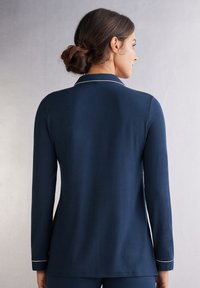 Mörkblå pyjamaströja med lång ärm och notchad krage, vit kantning längs kragen och manschetterna samt en avslappnad passform. Mjukt tyg med slät yta.
