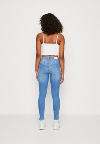 Blå skinny jeans med hög midja, texturerat jeansmaterial och bakfickor, tillsammans med en vit kortärmad topp och sneakers.