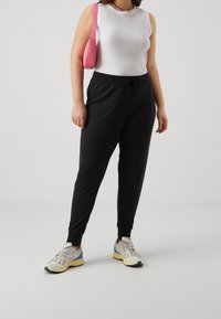 Černé jogger kalhoty s páskem na stažení, zúženými kotníky a bílým bezrukávovým topem. Doplněno růžovou kabelkou a barevnými teniskami.