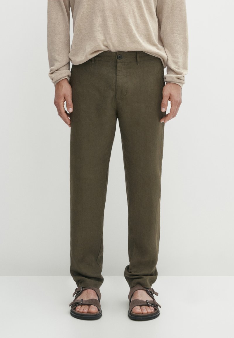 Pantaloni in lino verde oliva con vestibilità dritta, tasche frontali e chiusura con un bottone, abbinati a sandali marroni.