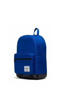 Sac à dos en tissu bleu avec une poche avant zippée, un fond noir et une poignée supérieure. Il présente une étiquette de logo et une texture lisse.