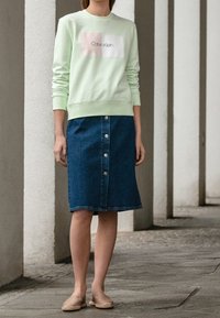 Světle mátově zelená mikina s bílým logem, doplněná tmavě modrou džínovou sukní s knoflíkovou přední částí a nedokončeným lemem. Celek doplňují béžové espadrilky.