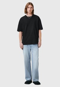 T-shirt nera oversize, jeans blu chiaro a gamba dritta dalla vestibilità ampia e ciabatte nere. Design elegante con un'estetica semplice.