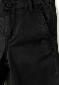 Pantalon en denim noir avec fermeture à bouton, poches avant et texture subtile. Les coutures sont visibles le long des coutures et des poches.