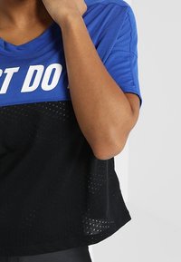 Camiseta deportiva azul y negra con cuello en V, que presenta una sección inferior texturizada en negro y letras blancas en negrita en la parte frontal.