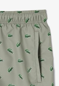 Groene shorts met elastische tailleband, voorzien van een herhaald krokodillenpatroon in donkerder groen met rode accenten. Glad textuur en zijzakken inbegrepen.