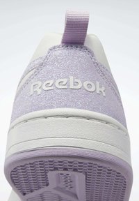 Lila glittrig sneaker med en vit gummisula. Har en tygslinga på hälen och embossad "Reebok"-logotyp på sidan.