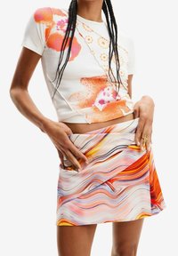 Vit ribbad kortärmad topp med orange och rosa blommönster, kombinerad med en flerfärgad virad minijurk med svängande mönster.