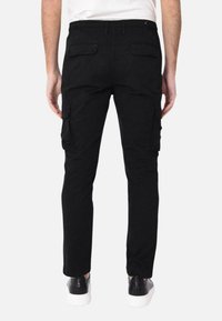 Pantaloni cargo neri con una vestibilità slim, dotati di tasche laterali, tasche posteriori e una cintura con un dettaglio elastico. Abbinati a sneakers nere.