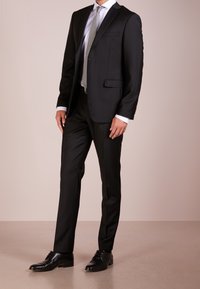 Svart skräddarsydd kostym med en enfaldig kavaj, slim-fit byxor, vit skjorta och grå slips. Avslutad med svarta läderskor.