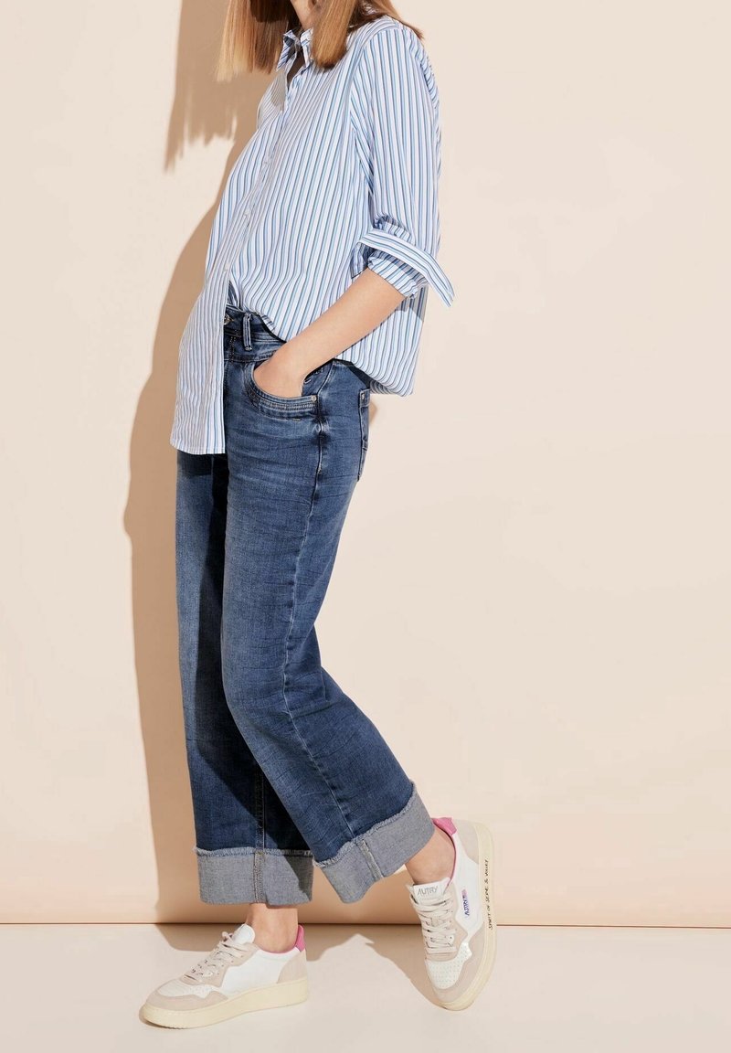 Randig blå och vit långärmad skjorta i kombination med löst sittande mörk denimjeans och krämfärgade sneakers med rosa detaljer.