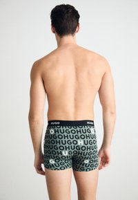 Schwarze und grüne Boxer-Shorts mit wiederholtem "HUGO"-Logo-Muster, weicher Stoff, enganliegendes Design, mittellange Oberschenkel, elastischer Taillenbund.