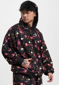 Black hoodie with colorful palm tree and sunset graphics. Features a kangaroo pocket and ribbed cuffs for a relaxed fit. Soft fabric texture.