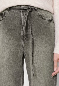 Pantalones de mezclilla gris con un corte relajado y una cintura ajustable con cordón. Presenta bolsillos delanteros y una textura deslavada con detalles de costura en contraste.