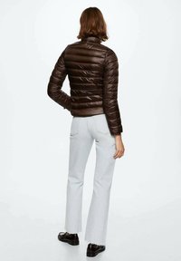 Brown puffer jacket with horizontal stitching, high collar, and long sleeves. Paired with light blue flared jeans and black shoes.