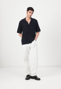 Cămașă navy cu mânecă scurtă, cu un model în romb și butoane, asortată cu pantaloni albi și pantofi negri, având o croială lejeră și guler.