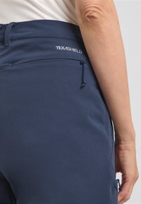 Pantaloni TEXASHIELD blu navy con una texture liscia, elastico in vita e cordoncino regolabile. Presentano una tasca laterale sul fianco sinistro.