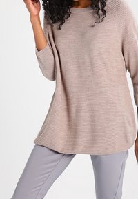 Pull beige clair en maille avec une coupe décontractée, manches raglan et ourlet côtelé. Associé à un pantalon slim gris clair.