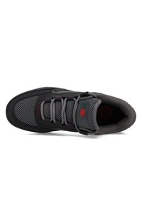 Schwarzer und grauer Sneaker mit Mesh-Obermaterial, gepolstertem Zungenbereich und strukturiertem Sohlenprofil. Verfügt über rote Akzente und graue Schnürsenkel.