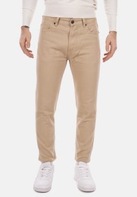 Chino in cotone beige con una vestibilità slim, dotati di chiusura a zip, cinque tasche, cuciture sottili e abbinati a sneaker bianche.