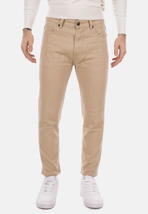 Chino in cotone beige con una vestibilità slim, dotati di chiusura a zip, cinque tasche, cuciture sottili e abbinati a sneaker bianche.