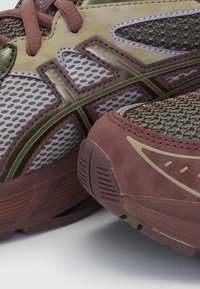 Scarpe da ginnastica in rete con tonalità verdi e marroni, caratterizzate da un design a motivi, accenti rinforzati e una suola texturizzata color bordeaux.