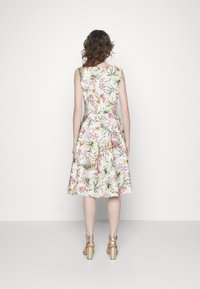 Robe florale avec un corsage ajusté et une jupe évasée, faite de tissu léger avec des couleurs pastel et des motifs de feuillage. Talons dorés visibles.
