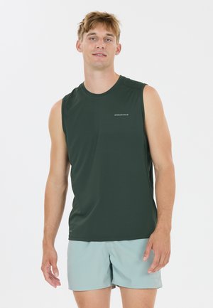 Jeune homme portant un débardeur de sport vert foncé et un short bleu clair, debout devant un fond blanc, regardant droit devant.