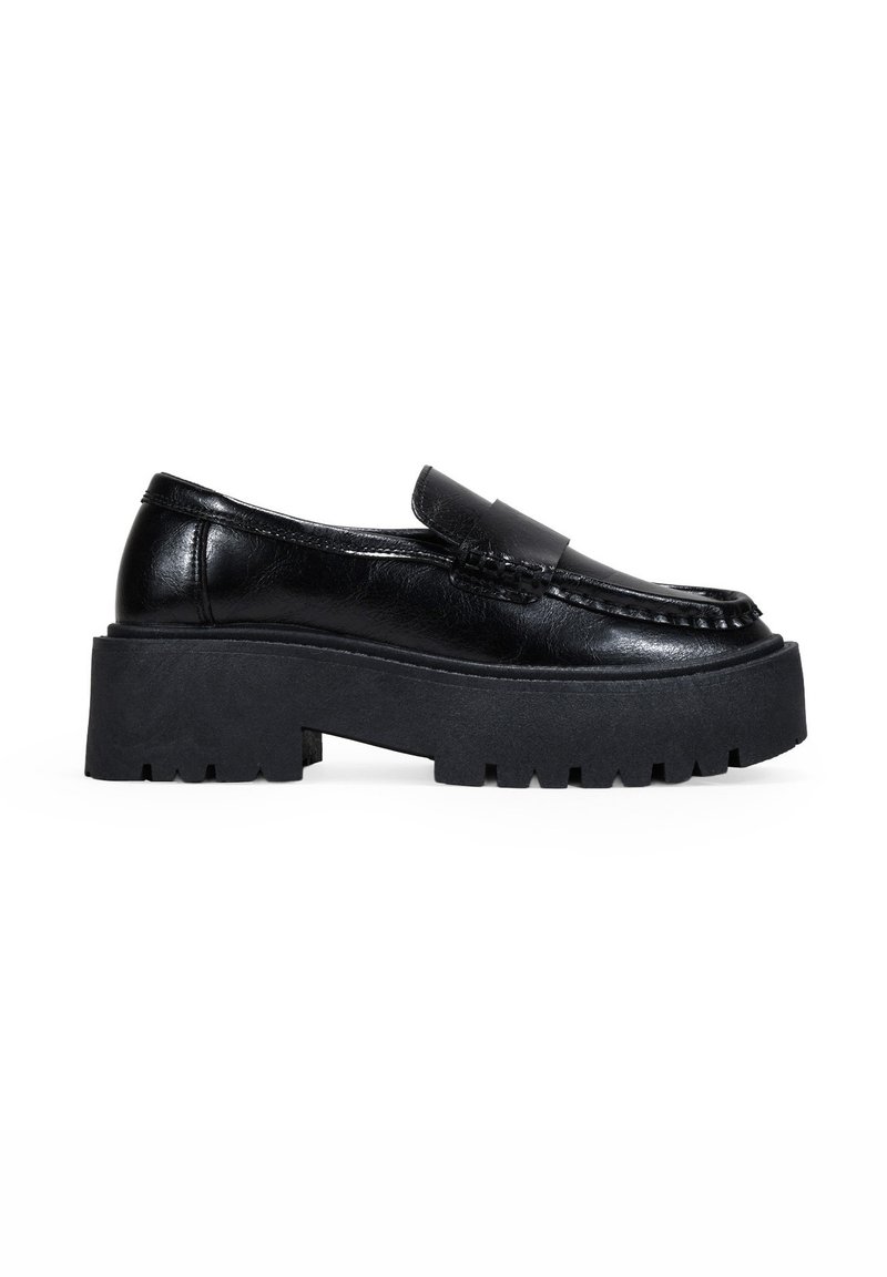 Mocasines de cuero negro con suela de goma gruesa, que presentan un detalle de costura y una correa ancha a lo largo del empeine.