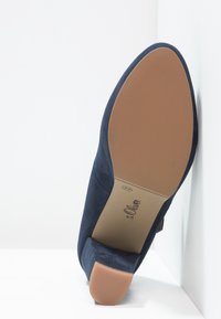 Chaussure à talon haute en daim bleu marine avec un bout arrondi et une semelle en caoutchouc beige, dotée d'un logo de marque embossé sur la semelle intérieure.