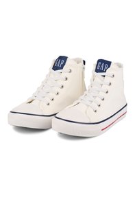 Witte hoge sneakers van canvas, met een marineblauwe bovenkant, witte veter en een gestreepte rubberen zool met rode en marineblauwe accenten.
