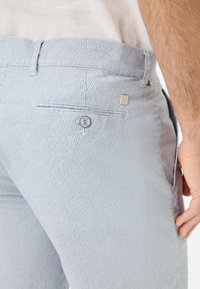 Pantaloni di cotone a righe blu e bianchi con una tasca posteriore con chiusura a pulsante e un piccolo'etichetta decorativa sulla cintura.