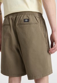 Olivgrüne Shorts mit elastischem Bund, zwei Gesäßtaschen und einem kleinen schwarzen Vans-Logoetikett am Bund. Glatte Textur.