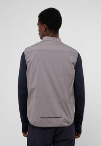 Leichter grauer Weste aus glattem, wasserabweisendem Material; mit hohem Kragen, einer Rückentasche und minimalistischen Designelementen.