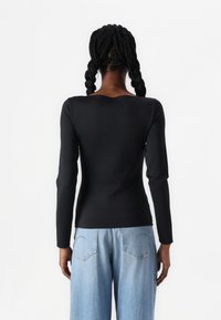 Black long-sleeve top with a scooped back neckline, made of smooth stretch fabric, paired with light blue wide-leg jeans.