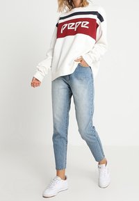 Felpa bianca con strisce bordeaux e blu navy, con logo "Pepe". Abbinata a jeans azzurri chiari e sneakers bianche.