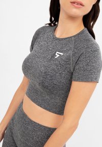 Cropped top grigio a maniche corte con design aderente, realizzato in tessuto texture, con un logo bianco sul davanti vicino al colletto.