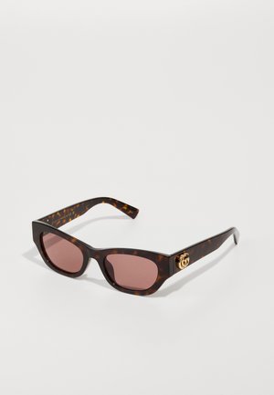 Cat-Eye-Sonnenbrille mit einem Gestell aus Schildpatt-Kunststoff, rosafarbenen Gläsern und einem goldenen Logo-Akzent an den Scharnieren. Glatte Textur und kantiges Design.