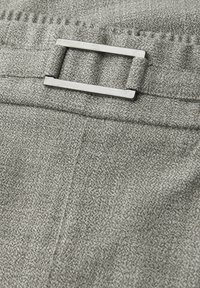 Nærbillede af tekstureret gråt stof med en rektangulær sølvbæltespænde og syede sømdetaljer.