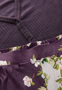 Purple textured fabric with a button at the neckline, layered over a floral-patterned purple and cream fabric with green accents.